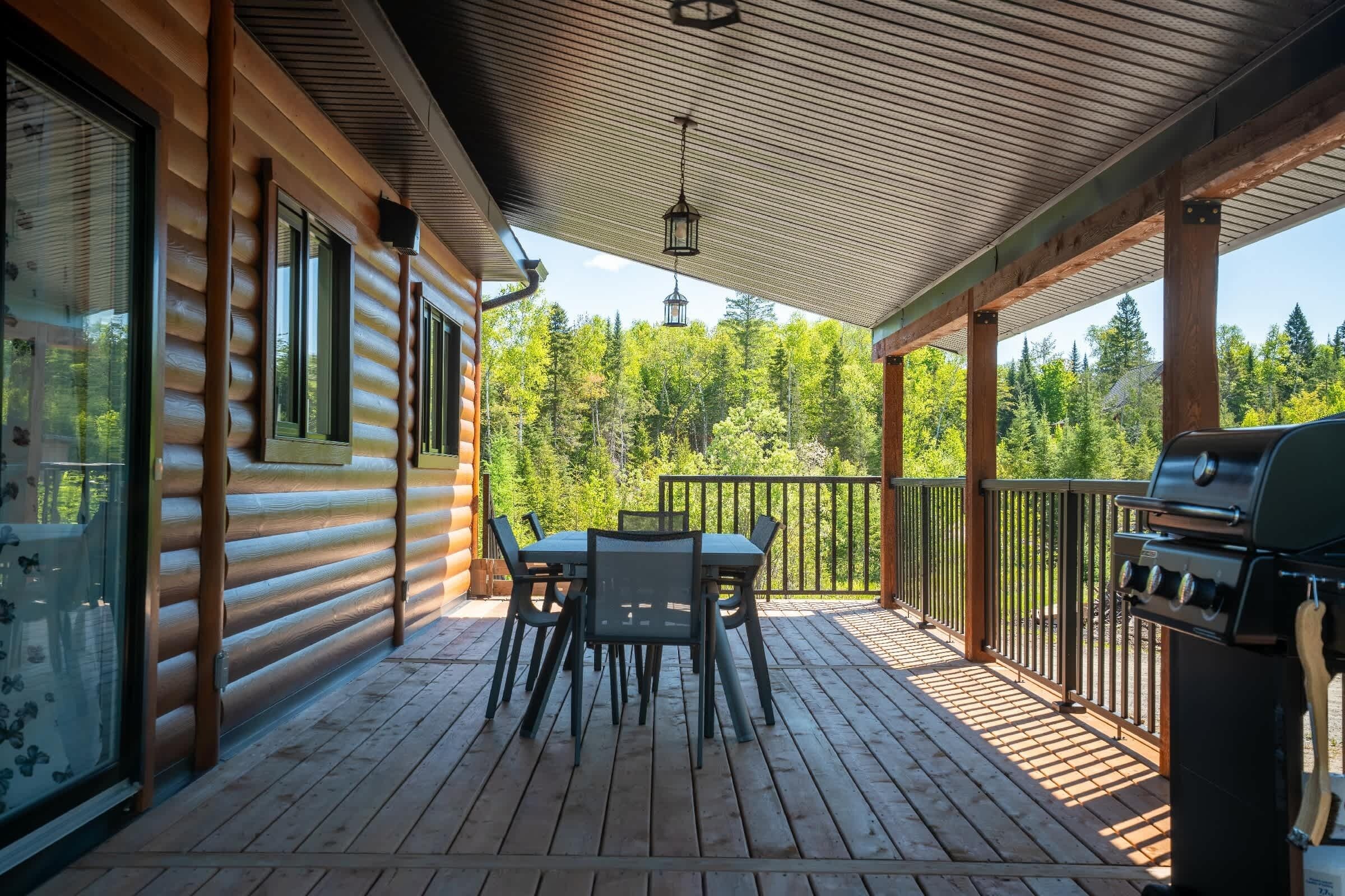 A wooden deck with a table and chairs, a grill, and a view of a forest.