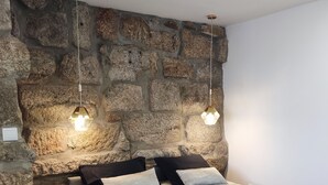 A bedroom with a stone wall, a bed with a gray blanket, and two hanging light fixtures. - Casa da Real Companhia (Lamego)