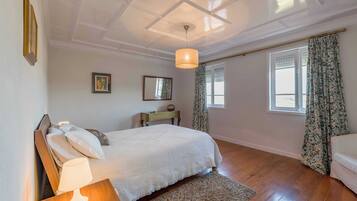 A bedroom with a bed, bedside lamp, wooden nightstand, and a small table with a lamp.