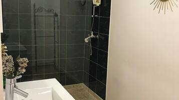 A bathroom with a white sink, a shower with black tiles, and a sunburst mirror on the wall.