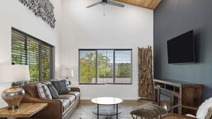 A modern living room with a brown leather sofa, a round coffee table, a fireplace, and a large window with blinds. - Modern 2-bedroom house with WiFi, AC in Kimberling City (Kimberling City)