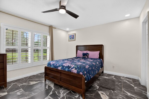 A bedroom with a bed, a ceiling fan, a window, and a door.