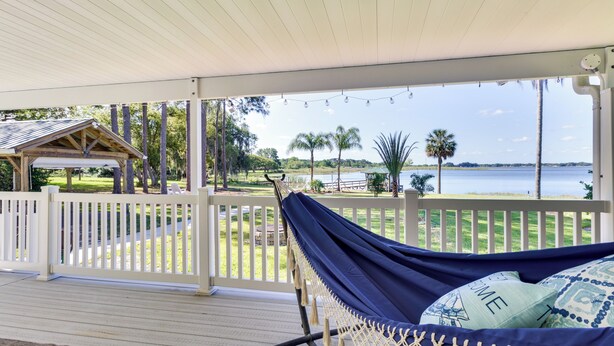 Una hamaca en una terraza de madera con vista a un lago y palmeras.