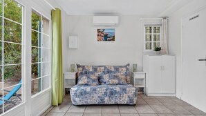 Een kamer met een bed, een raam met gordijnen, een wandairconditioner, een tafeltje met een plant en een kast.