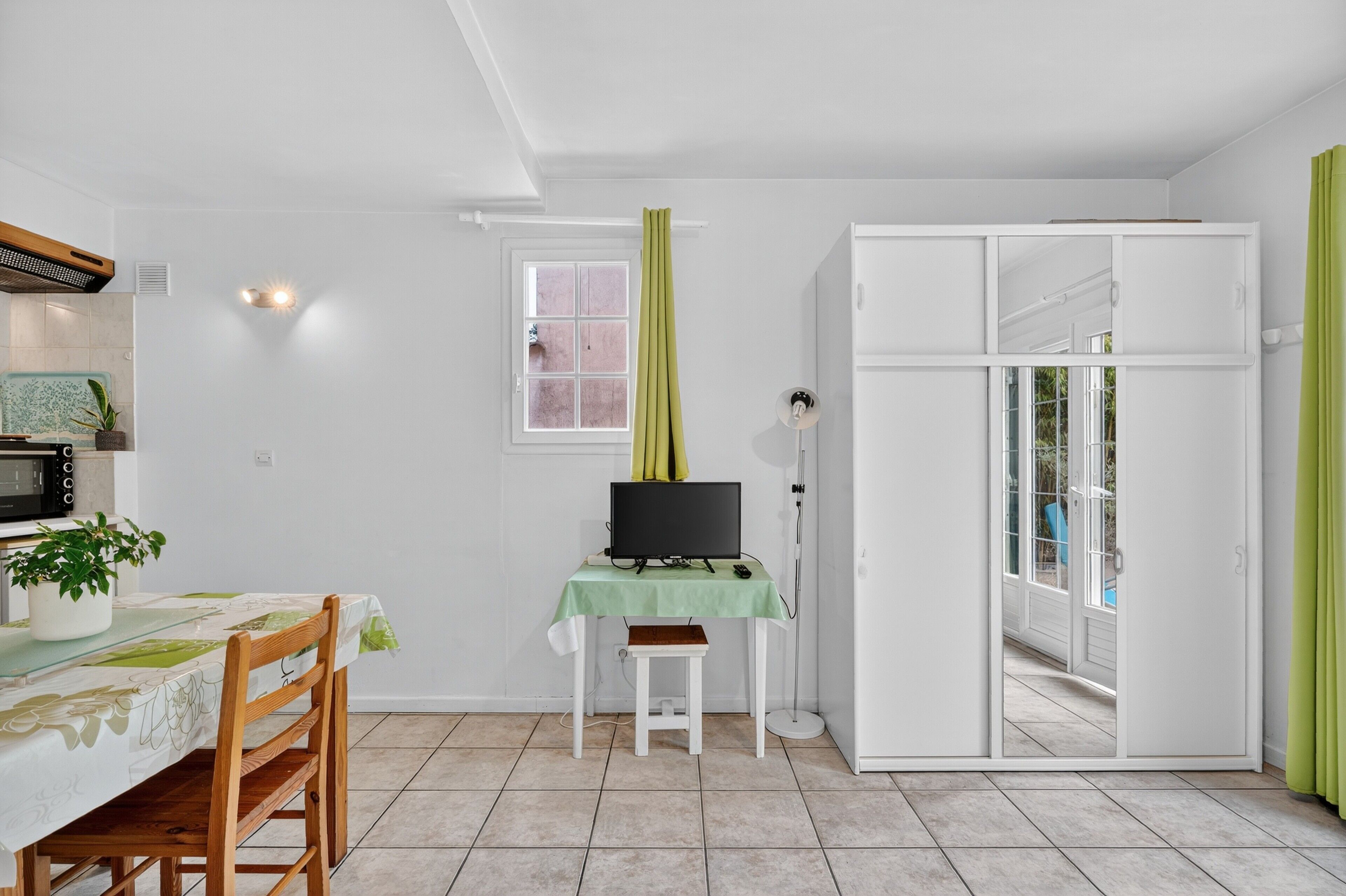 A room with a dining table, a TV on a stand, a small stool, a cabinet, and a sliding door leading to a balcony.