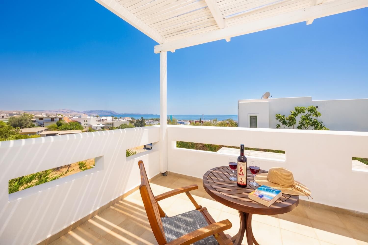 Een balkon met uitzicht op zee, een tafel met een fles wijn, twee glazen en een boek.