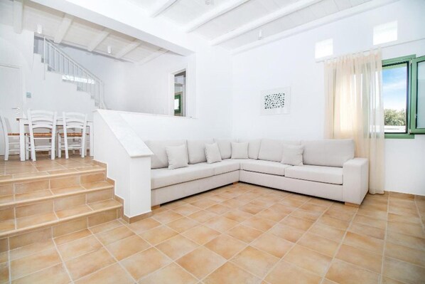 Amplia sala de estar con un sofá seccional blanco, una escalera y un comedor con sillas blancas.