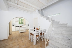 A spacious interior with a dining area, a kitchen, and a marble staircase.