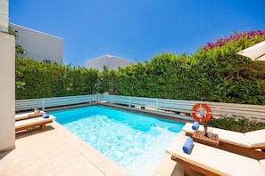 A swimming pool with lounge chairs and a lifebuoy, surrounded by greenery and a white fence.