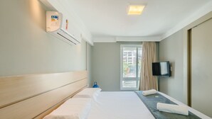 Et hotelværelse med seng, fjernsyn, et vindue med gardiner og en klimaanlæg.