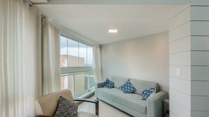 En moderne stue med sofa, lænestol og et stort vindue med gardiner.