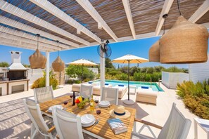 An outdoor dining area with a pool, white furniture, and hanging wicker lamps. - Villa Pollux - Two Bedroom Villa, Sleeps 4 (Gennadi)