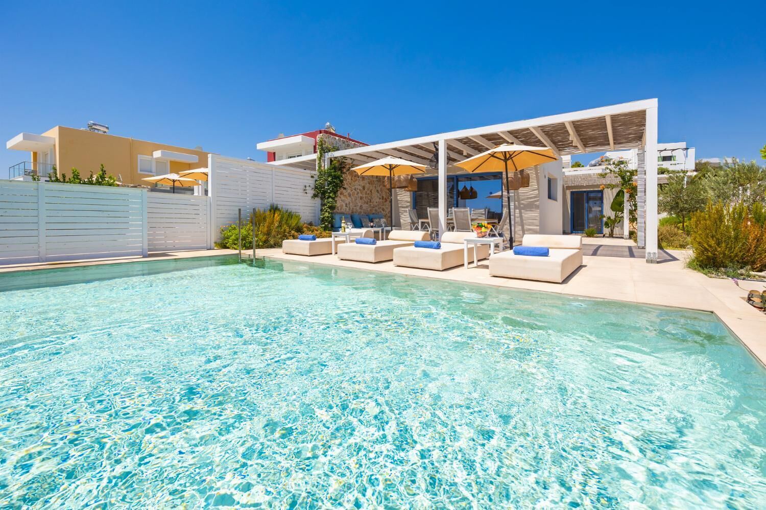 Une piscine entourée de chaises longues et de parasols, le tout bordé d’un bâtiment moderne à la façade blanche.