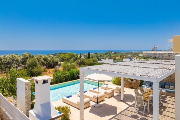 A rooftop pool area with a view of the sea, outdoor seating, and a pergola.