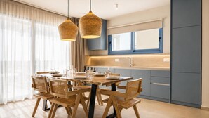 A modern kitchen with a dining area, featuring a wooden table and chairs, a built-in oven, and a window with curtains. - Villa Pollux - Two Bedroom Villa, Sleeps 4 (Gennadi)