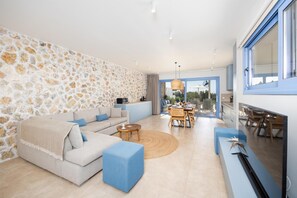 Un salon moderne avec un mur en pierre, un canapé, une table basse et un coin repas comprenant une table et des chaises.