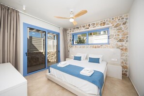 A bedroom with a bed, a ceiling fan, a stone wall, and a view through a window.