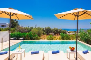 A poolside area with lounge chairs, umbrellas, and a view of the sea.