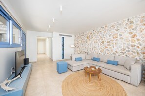 Una sala de estar moderna con una pared de piedra, un sofá seccional, una mesa de centro y un televisor sobre un mueble.