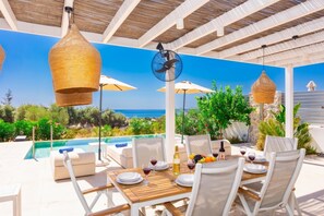 An outdoor dining area with a pool, white furniture, and a view of the sea.
