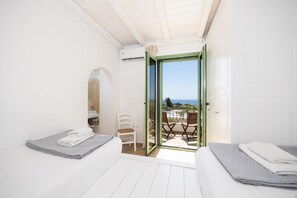 A room with two beds, a chair, and a balcony with a view.