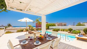 Un espace extérieur abrité, aménagé pour les repas, avec une piscine et une vue sur la mer.