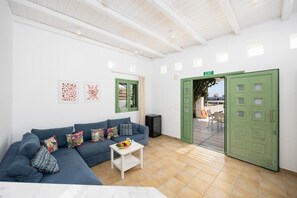 Ein Zimmer mit einem blauen Sofa, einem kleinen weißen Tisch mit einer Obstschale, einer grünen Tür und einer weißen Wand mit gerahmten Bildern.