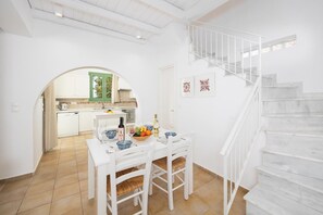 Ein helles Interieur mit einem Esstisch für zwei Personen, einer Küche im Hintergrund und einer Treppe.