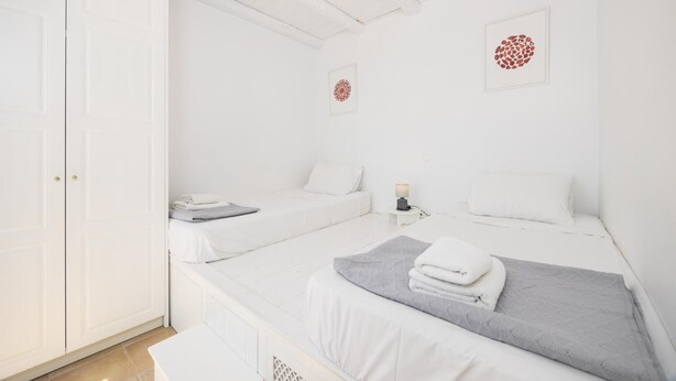 Une chambre avec deux lits, une armoire blanche et une petite table avec une lampe.