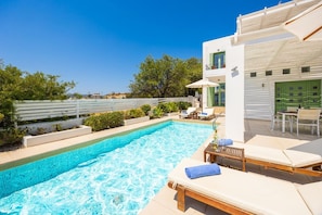 Ein Pool mit Liegestühlen und einem Tisch, umgeben von einem weißen Zaun und Grünpflanzen.