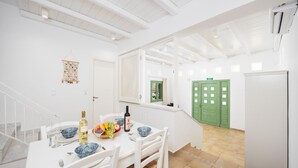 Un coin repas avec une table blanche dressée pour quatre personnes, une porte verte et un escalier menant à un autre niveau.