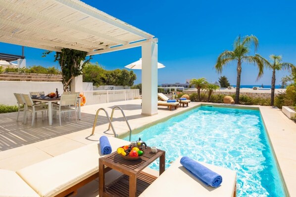 A swimming pool with lounge chairs and a table with fruit and a towel.