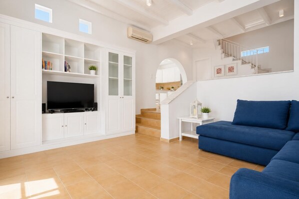 Een moderne woonkamer met een flatscreen televisie, witte kasten, een blauwe bank en een trap.