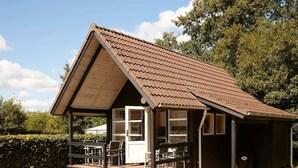 A small, single-story wooden cabin with a pitched roof, a porch with seating, and a door leading to the interior. - 6 Person Holiday Park Home in Bryrup (Bryrup)