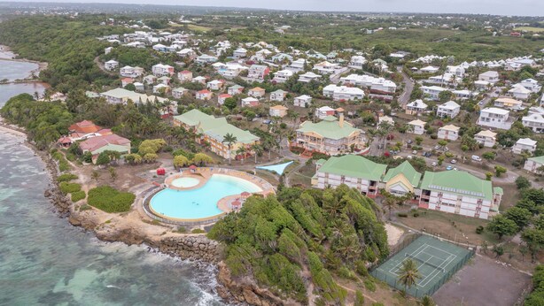 An aerial view of a coastal residential area with houses, a swimming pool, and a tennis court. - La Désirade, Air-conditioned bedroom in a private estate with beach access & pool (Saint François)
