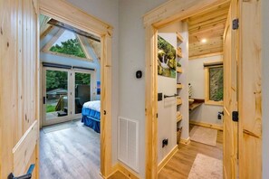 A wooden interior with a sliding glass door leading to an outdoor area, a bed with a blue bedspread, and a shelf with decorative items.