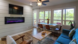 A modern living room with a fireplace, dining area, and large windows. - Modern Cabin, Close to Dahlonega & Wineries, View, Hot Tub, Pet Friendly (Dahlonega)