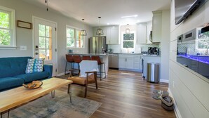 A modern kitchen with white cabinets, a stainless steel refrigerator, and a built-in oven. There is a dining area with a blue sofa and a wooden table. - Modern Cabin, Close to Dahlonega & Wineries, View, Hot Tub, Pet Friendly (Dahlonega)