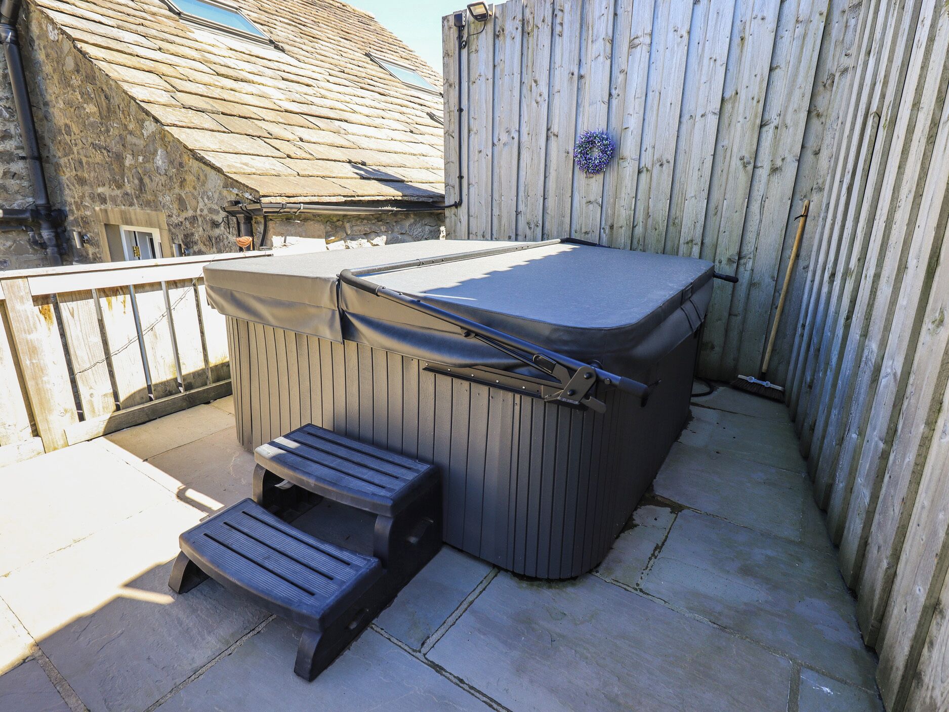A hot tub with steps, a wooden deck, and a wooden fence.
