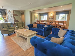 A living room with a sectional sofa, a coffee table, and a dining area with wooden chairs and a table. - Fogga Croft (Skipton)