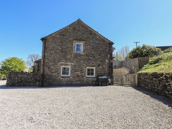 A stone building with two windows and a gravel driveway.