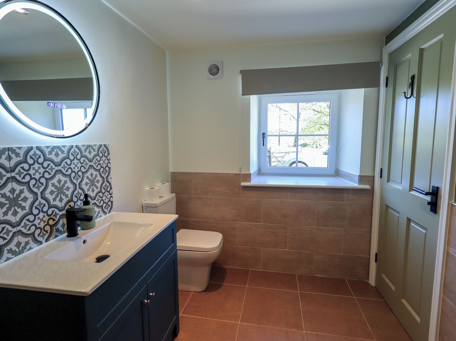 A bathroom with a toilet, a sink with a mirror, patterned tiles, a window, and a door.