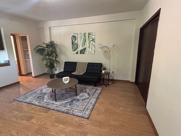Un salón con un sofá oscuro, una mesa de centro, una planta grande en maceta y una lámpara de pie.