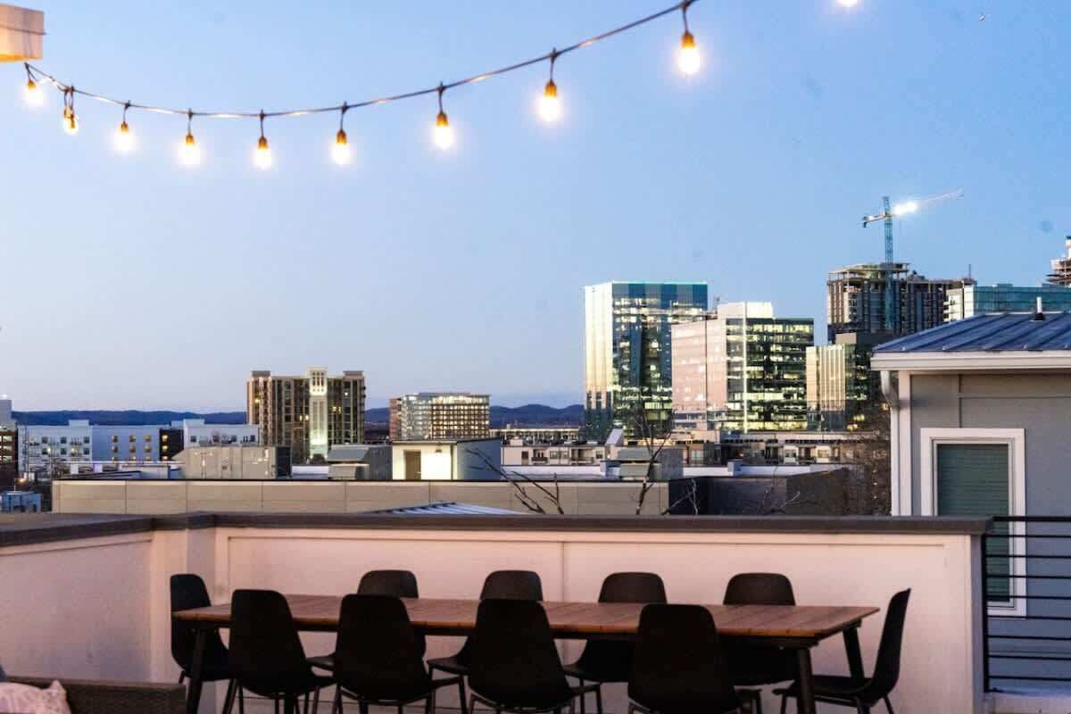 A rooftop terrace with a dining table and chairs, overlooking a cityscape with modern buildings and a construction crane.