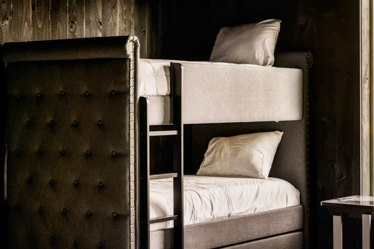 A bunk bed with a ladder, a pillow on the top bunk, and a wooden wall in the background.