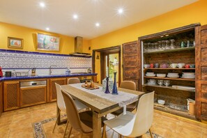 Une cuisine équipée d’une table à manger, de chaises, d’une cuisinière et d’une étagère où sont rangés la vaisselle.