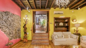 A room with a staircase leading to a balcony, a white sofa, a wooden coffee table, and a chandelier. - Casa Carmen – Historic Holiday Home with Teide and Sea Views in La Matanza de Acentejo (La Matanza de Acentejo)