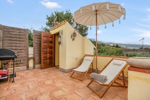 Une terrasse avec deux chaises longues, un barbecue et un parasol.