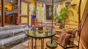 A glass table with a metal frame, a striped sofa, and a potted plant in a sunlit room with a stone staircase. - Casa Carmen – Historic Holiday Home with Teide and Sea Views in La Matanza de Acentejo (La Matanza de Acentejo)