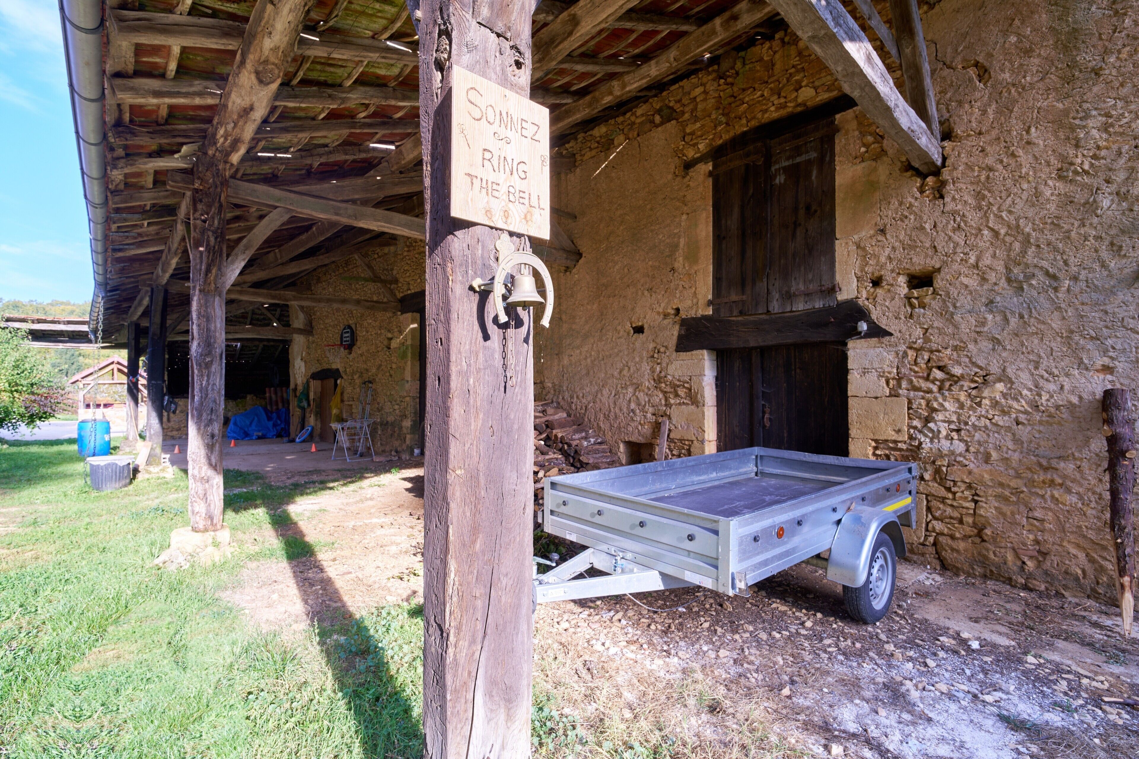 A rustic building with a wooden structure, a bell, and a sign that reads 'SONNEZ RING THE BELL'.